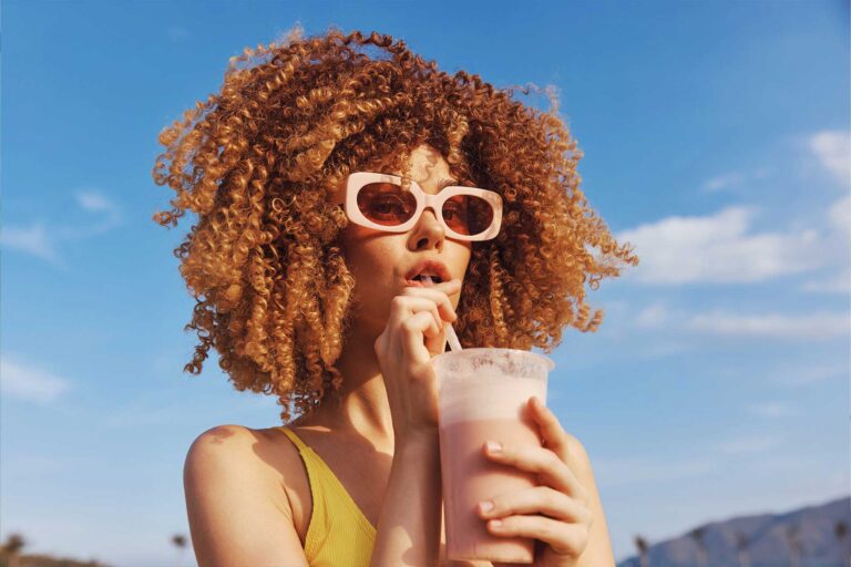 woman with curly hair enjoying a smoothie on a sun 88Z62G9